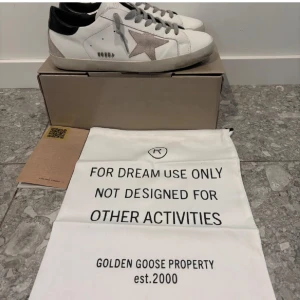 Golden Goose Super-Star sneakers - Snygga vita Golden Goose Super-Star sneakers med en grå stjärna på sidan och svarta detaljer. Skorna har en klassisk design med snörning och är tillverkade i Italien. Endast använd 1 gg för o testa men var för stora!!! Kvitto finns! 