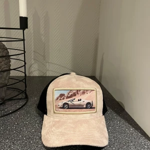 Beige och svart keps med bilmotiv - Snygg keps i beige och svart med ett coolt bilmotiv framtill. Kepsen har ett justerbart spänne bak och meshmaterial på sidorna för extra ventilation. Perfekt för en avslappnad stil. Kan gå ner i pris vid snabb och smidig affär 