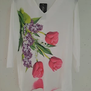 Vit blus med blommönster - Säljer en vit blus från Luca d'Agostino med ett vackert blommönster i rosa och lila. Blusen har en v-ringad hals och trekvartsärmar, perfekt för en stilren look.