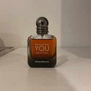 Stronger With You Absolutely från Emporio Armani - Säljer en elegant parfymflaska av Stronger With You Absolutely från Emporio Armani. Flaskan har en stilren design med en gradient från mörk till ljusbrun och en metallisk kork. Perfekt för den som vill ha en sofistikerad doft. 50ml max 10 sprut så cirka 48-49ml kvar. Skriv för frågor nypris 1000kr köpt på kicks.