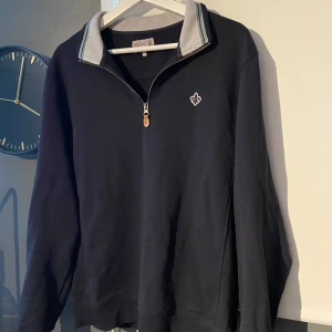 Mörklbå quarter zip från Morris - Snygg Mörkblå tröja från Morris med dragkedja och en stilren logga på bröstet. Tröjan har en grå krage som ger en fin kontrast. Tröjan är i mycket bra skick!