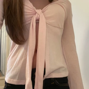 Ljusrosa knyttopp från Gina tricot  - Säljer en söt ljusrosa topp från Gina Tricot. Toppen har långa ärmar och en knytning framtill som gör en fin liten rosett. Den är knappast använd och har inga fläckar. Funkar att ha en tröja under eller bara ha den som den är!