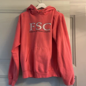 Rosa hoodie med FSC-tryck - Säljer en rosa hoodie från Champion med FSC Florida Southern College-tryck på bröstet. Tröjan har en klassisk känguruficka och en justerbar huva. Perfekt för en avslappnad stil.