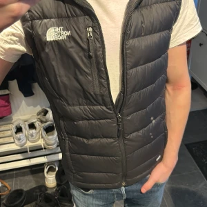 Svart dunväst från The North Face - Säljer en svart dunväst från The North Face med dragkedja och logga på bröstet. Nypris cirka 1700, skriv om du har minsta fundering