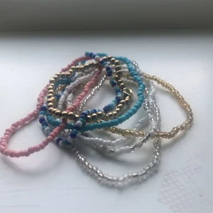 Färgglada pärlarmband - Säljer ett set med färgglada pärlarmband i olika färger som rosa, blå, vit, guld och silver. Perfekta för att mixa och matcha till olika outfits. Armbanden är elastiska och passar de flesta handleder.