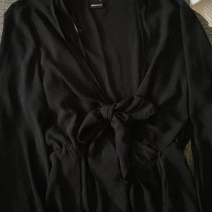 Svart blus från Gina Tricot - Snygg svart blus från Gina Tricot med knytning vid bröst. Blusen har långa utsvängda ärmar och en elegant v-ringning. Perfekt för en stilren look.