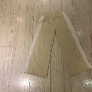 Beige byxor med vita detaljer - Snygga beige byxor med vita sidopaneler. Perfekta för en avslappnad stil. Byxorna har en loose passform och är tillverkade i ett bekvämt material.