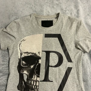 Grå t-shirt med dödskalle från Philipp Plein - Snygg grå t-shirt från Philipp Plein med ett stort tryck av en dödskalle och bokstäver på framsidan. Använd lite grann men inte mycket sp i bra skick.