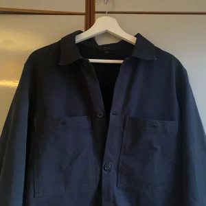 Mörkblå overshirt från COS - Snygg mörkblå overshirt från COS med knappar framtill och två bröstfickor. Perfekt för både vardag och mer uppklädda tillfällen. Typ helt ny använd typ 2-3 gånger. Köpt för ca 700-800 tror ej dem säljs längre. Kan gå ner i pris 