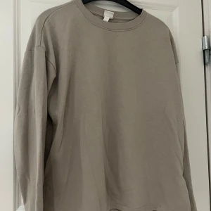 Beige långärmad tröja från H&M - Säljer en stilren beige långärmad tröja från H&M. Perfekt för en avslappnad look med sin enkla design och mjuka material. Tröjan har en rund hals och slitsar på sidorna för extra komfort. Passar bra till både jeans och joggers. Lite sliten vid halsen. Är lite mörk beige i verkligheten.