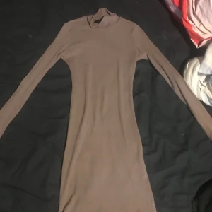 Beige ribbad klänning från Kikiriki - Säljer en stilren beige ribbad klänning från Kikiriki i storlek XS. Klänningen har en tight passform och långa ärmar, perfekt för en elegant look. Den höga halsen ger en extra touch av sofistikation.