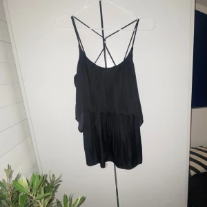 Svart ärmlös topp från KappAhl - Snygg svart ärmlös topp från KappAhl med tunna axelband och en luftig design. Perfekt för varma dagar eller som ett lager under en jacka. Toppen har en elegant och enkel stil som passar till många olika outfits.