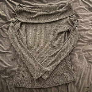 Grå ribbad offshoulder tröja från Gina Tricot - Snygg grå ribbad offshoulder tröja från Gina Tricot. Perfekt för en stilren look med långa ärmar och en bekväm passform. Ett måste i garderoben för den som gillar trendiga plagg.