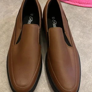 Bruna loafers från Stepside Comfort - Snygga bruna loafers från Stepside Comfort i skinn. De har en stilren design utan snörning och en bekväm sula för extra komfort. Perfekta för en avslappnad men ändå elegant look.