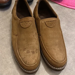 Bruna loafers i skinn - Säljer ett par bruna loafers i skinn med en stilren design. Skorna har en diskret söm och en robust sula för extra komfort. Perfekta för en avslappnad men ändå stilfull look.