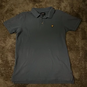 Blå pikétröja från Lyle & Scott - Säljer en snygg blå pikétröja från Lyle & Scott Junior. Tröjan har korta ärmar och en klassisk krage med knappar. Skick 8/10. Använd fåtal gånger. Skriv vid minsta fundering.