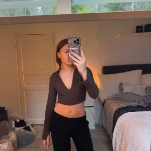 Svart croppad polotopp - Snygg mörk brun  croppad” korsett liknande  skjorta” med långa ärmar och djup v-ringning. Perfekt för en trendig look. Säljer då den är lite liten i armarna. 