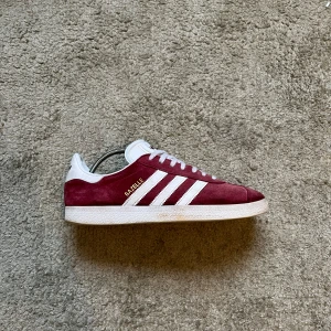 Adidas Gazelle - Ett par vinröda adidas gazelle. Storlek 41 1/3. Dom är använda och förekommer därför små defekter men ändå i hyfsat fint skick. Hör av dig om du har fler frågor!