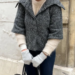 Grå kappa i ull - Säljer en snygg grå kappa med fiskbensmönster. Den har en bred krage och trekvartsärmar, perfekt för höst och vår. Den är gjord av ull och har knappar framtill. Superchic och lätt att matcha med olika outfits! Ganska nopprig men annars i bra skick. Köpt i Paris 💋