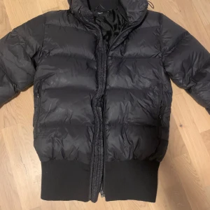 Svart dunjacka från Filippa K - Säljer en snygg svart dunjacka från Filippa K i mycket bra skick. Jackan är perfekt för vintern med sitt varma gåsdunfoder (80/20) och har en stilren design med dragkedja. Yttermaterialet är i polyamid och fodret i polyester. Passar perfekt för kalla dagar!