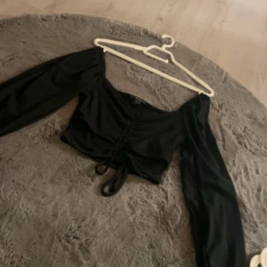 Svart ribbad topp från Amisu - Snygg svart ribbad topp från Amisu i storlek M. Den har långa ärmar och en cool snörning framtill som ger en unik look. Perfekt för både vardag och fest!