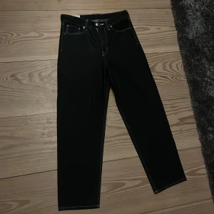 Svarta byxor från H&M - Säljer ett par mörka denim byxor från H&M med loose fit. Byxorna har en klassisk design med fem fickor och knappgylf. Perfekta för en avslappnad stil. Har inte använt en ända gång så är nya. Köpt för mindre än en månad sedan för 349 