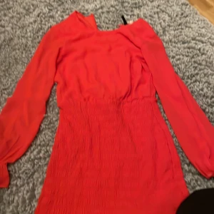 Röd klänning  - Snygg röd klänning  med långa ärmar och en smickrande passform. Klänningen har en elastisk midja och är tillverkad i ett mjukt material som ger en bekväm känsla. Perfekt för att sticka ut med sin klara färg.