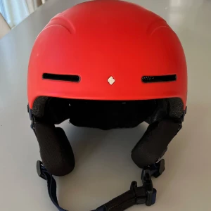 Skidhjälm, Blaster Helmet Junior, från Sweet Protection - Blaster Helmet Junior från Sweet Protection i storlek S/M (53-56 cm).. Hjälmen har en stilren design med justerbart spänne och ventilationshål för extra komfort. Skyddad med Impact Shields och ABS hard-shell förstärkning. Kommer med en praktisk förvaringspåse och extra passkuddar.