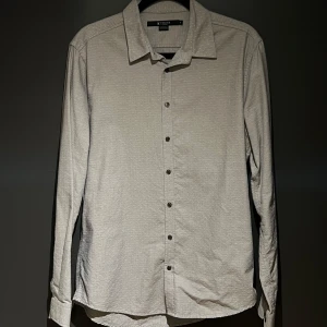 Grå långärmad skjorta från Tiger of Sweden - Snygg och stilren vit skjorta från Tiger of Sweden. Skjortan har en klassisk krage och knappar framtill. Perfekt för en elegant look.