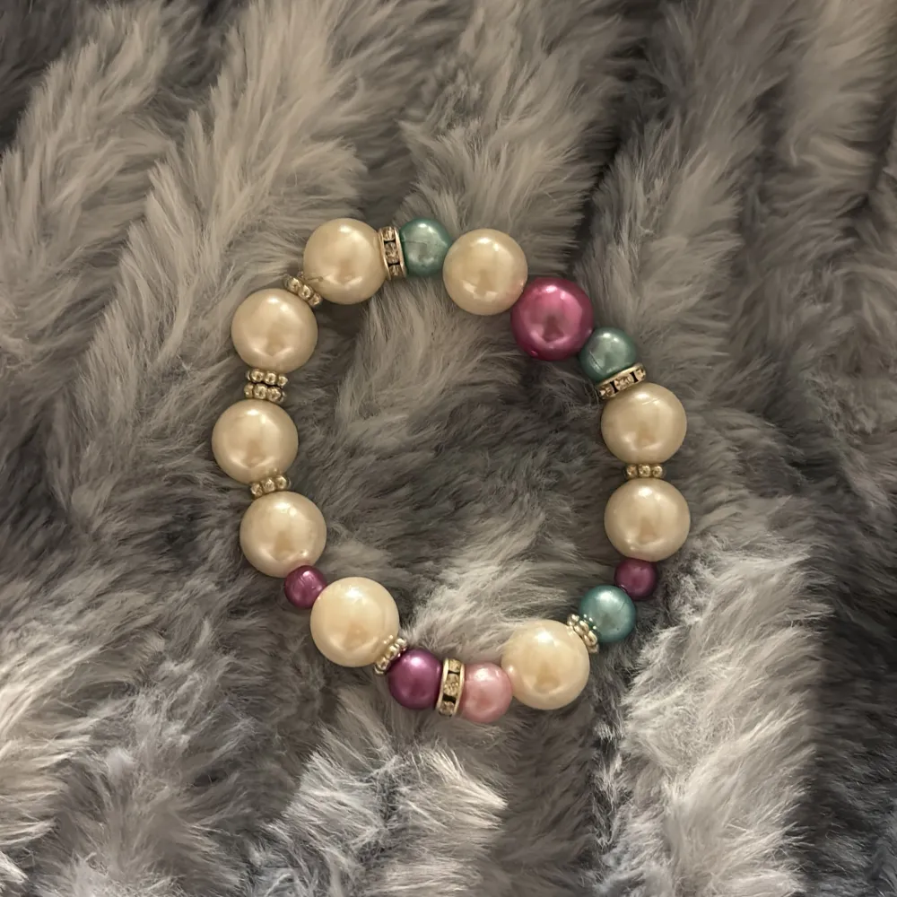 Charmigt armband med stora pärlor i vitt, rosa och blått. Pärlorna är separerade av små glittriga detaljer som ger en extra touch av elegans. Perfekt för att liva upp vilken outfit som helst!. Asusteet.