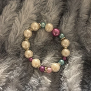 Färgglatt pärlarmband - Charmigt armband med stora pärlor i vitt, rosa och blått. Pärlorna är separerade av små glittriga detaljer som ger en extra touch av elegans. Perfekt för att liva upp vilken outfit som helst!