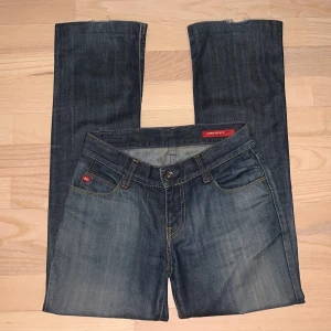 Blå jeans från Miss Sixty - Snygga blå lågmidjade jeans från Miss Sixty med klassisk femficksdesign och guldfärgade sömmar. De har en knapp och dragkedja framtill samt en läderpatch. Jag är ca 162 cm. Midja = 35 cm (tvärs över)