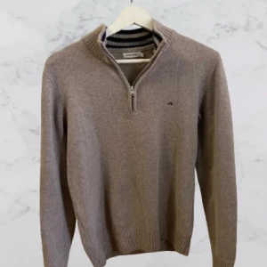 Beige tröja med dragkedja från J.Lindberg - Snygg beige tröja från J.Lindberg med halv dragkedja och ribbad krage. Perfekt för kyligare dagar med sin stilrena design och långa ärmar.