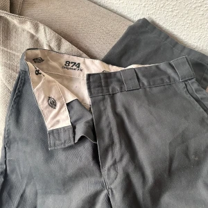 Grå byxor från Dickies - Säljer ett par klassiska grå byxor från Dickies, modell 874 Original Fit. Byxorna har en stilren design med hällor för bälte och en diskret logga på baksidan. Perfekta för en avslappnad men ändå snygg look. Passar mig som är S