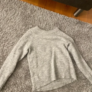 Grå stickad tröja från Selected Femme - Mysig grå stickad tröja från Selected Femme. Perfekt för kyliga dagar med sin mjuka och varma känsla. Tröjan har en enkel design med långa ärmar och ribbade kanter. Passar både till vardags och lite finare tillfällen. 🧶✨ använd fåtal ggr!