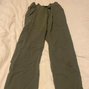 Olivgröna byxor från QED London - Säljer ett par olivgröna byxor från QED London i storlek S. De har en loose passform med elastisk midja och knappar framtill. Perfekta för en avslappnad stil och kan matchas med en enkel t-shirt eller tröja. Materialet känns mjukt och bekvämt.