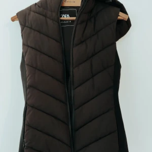 Svart väst från Zara - Säljer en svart väst från Zara i mycket bra skick. Västen har en dragkedja framtill och en mysig luva. Perfekt för höst och vinter när du vill hålla dig varm och stilren. Passar till både vardag och lite mer uppklädda tillfällen.