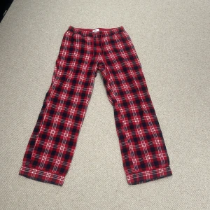 Helt oanvända röda rutiga byxor från Twilfit - Säljer ett par mysiga röda rutiga byxor från Twilfit. Perfekta för en avslappnad dag hemma eller som pyjamasbyxor. De har en bekväm passform med snörning i midjan för justerbarhet. Materialet känns mjukt och skönt mot huden.
