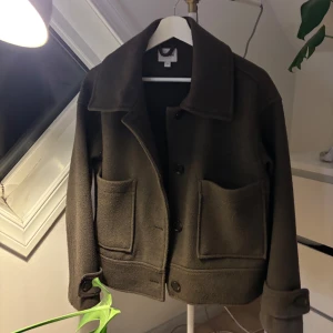 Brun kappa från Kappahl - Säljer en snygg brun kappa från Kappahl i storlek S. Jackan har stora fickor framtill och knäpps med knappar. 