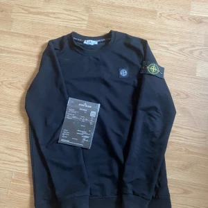 Svart tröja från Stone Island - Säljer en svart långärmad tröja från Stone Island. Den har deras ikoniska märke på ärmen och bröstet. Perfekt för en stilren och avslappnad look. Tröjan är i mycket bra skick och passar perfekt till både vardag och fest.