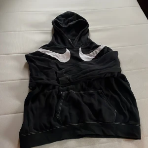 Svart hoodie från Nike - Säljer en svart hoodie från Nike i bra skick. Den har en stor vit logga på bröstet och en praktisk magficka. Perfekt för höst och vinter, och den är superbekväm med långa ärmar och mjukt material. Passar både till vardags och träning!