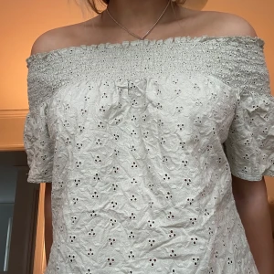 Vit offshoulder blus - Charmig vit offshoulder blus med broderade detaljer och korta ärmar. Perfekt för en somrig look med sin luftiga design och romantiska stil.
