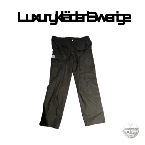 Svarta byxor från Carhartt - Säljer ett par svarta byxor från Carhartt med praktiska fickor och en avslappnad passform. Perfekta för en stilren och bekväm look. Tillverkade i en bomulls- och polyesterblandning.