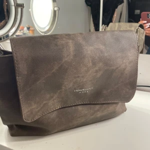 Brun axelväska från Fashion & Bags - Snygg brun axelväska i skinn från Fashion & Bags. Väskan har en kedjerem och ett stort huvudfack med gott om plats för dina saker. Perfekt för en stilren look. oanvänd 