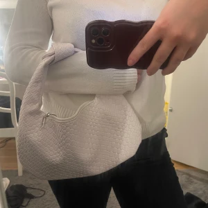 Vit axelväska med knut - Snygg vit axelväska med ett flätat mönster och praktisk dragkedja. Aldrig använd