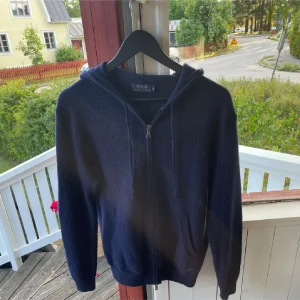 Mörkblå hoodie från Ralph Lauren - Säljer en snygg mörkblå hoodie från Ralph Lauren med dragkedja framtill. Tröjan är stickad i merinoull ull och har en klassisk design med huva och långa ärmar. Perfekt för kyliga dagar då den är extremt varm.