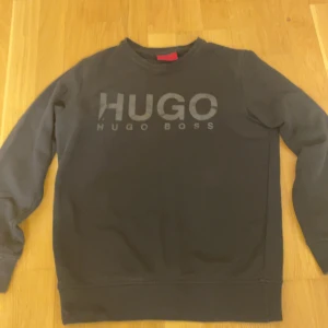 Svart tröja från Hugo Boss - Säljer en stilren svart tröja från Hugo Boss med deras logga tryckt på framsidan. Tröjan har långa ärmar och en klassisk rund halsringning. Perfekt för en avslappnad och trendig look🖤.