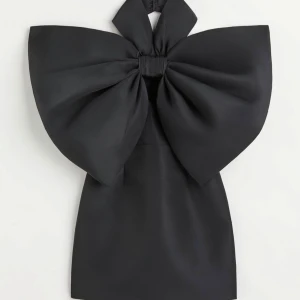 Svart klänning med stor rosett från H&M Innovation - Snygg svart klänning från H&M med en imponerande stor rosett framtill. Klänningen har en unik design som verkligen sticker ut och är perfekt för festliga tillfällen. Den är axelbandslös och har en kort längd. Storlek 34. Endast använd en gång då den är lite för liten för mig som vanligtvis har syl 36. Normal i storleken. Nypris 999kr säljer den 350kr. Köparen står för frakt alternativt avhämtning. 