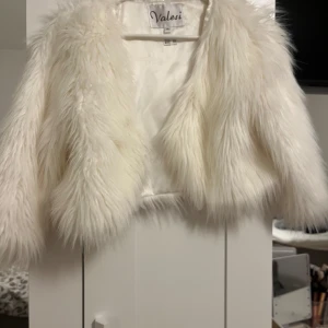 Vit pälsjacka från Valesi - Säljer en fluffig och stilren vit pälsjacka från Valesi. Jackan har en öppen design och är perfekt för att ge en lyxig touch till din outfit. Den är mjuk och bekväm att bära.