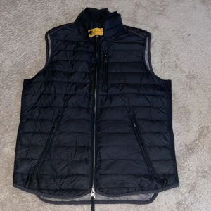 Mörkblå/dunväst från Parajumpers - Säljer en mörk navy blue dunväst från Parajumpers i mycket bra skick. Västen har en dragkedja framtill och en snygg gul detalj vid kragen. Perfekt för höst och vår när du vill hålla dig varm men ändå se stilren ut. Passar både till vardags och lite finare tillfällen. Passar S-M.